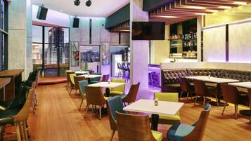 Um restaurante moderno com área de bar, diversas opções de assento incluindo mesas e cabines, e amplas janelas com vista para a cidade.
