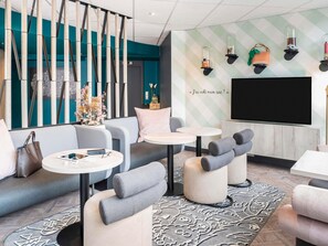 A modern hotel lobby with a sofa, two round tables, a TV, and decorative wall lights. - ibis Styles Sceaux Paris Sud (Sceaux)