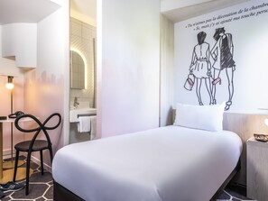 A hotel room with a bed, a desk, a chair, a mirror, and a wall decoration. - ibis Styles Sceaux Paris Sud (Sceaux)