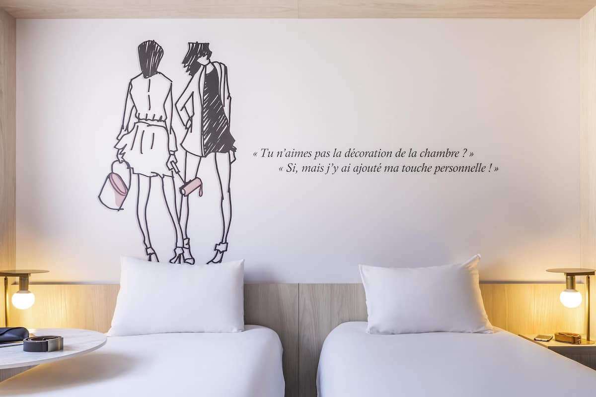 A hotel room with two beds, a wall decoration of a couple, and a quote in French.
