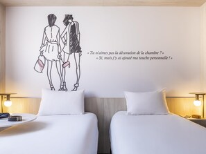 Een hotelkamer met twee bedden, een decoratie van een stel en een citaat in het Frans.