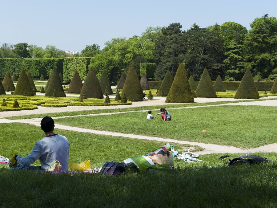Un parc avec des haies soigneusement taillées et une personne assise sur l’herbe.