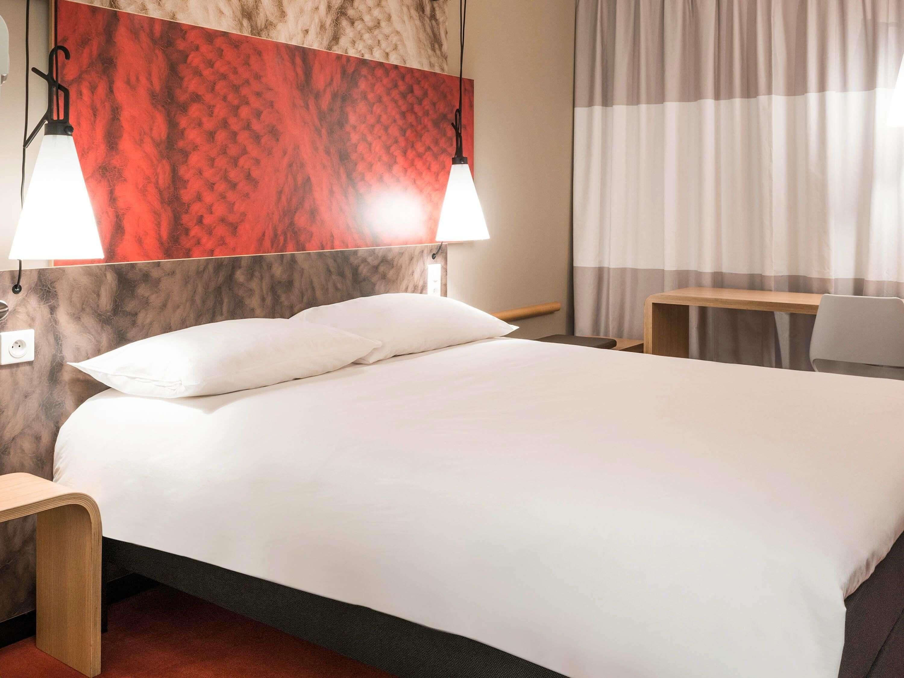A hotel room with a bed, two bedside lamps, a desk, and a chair.