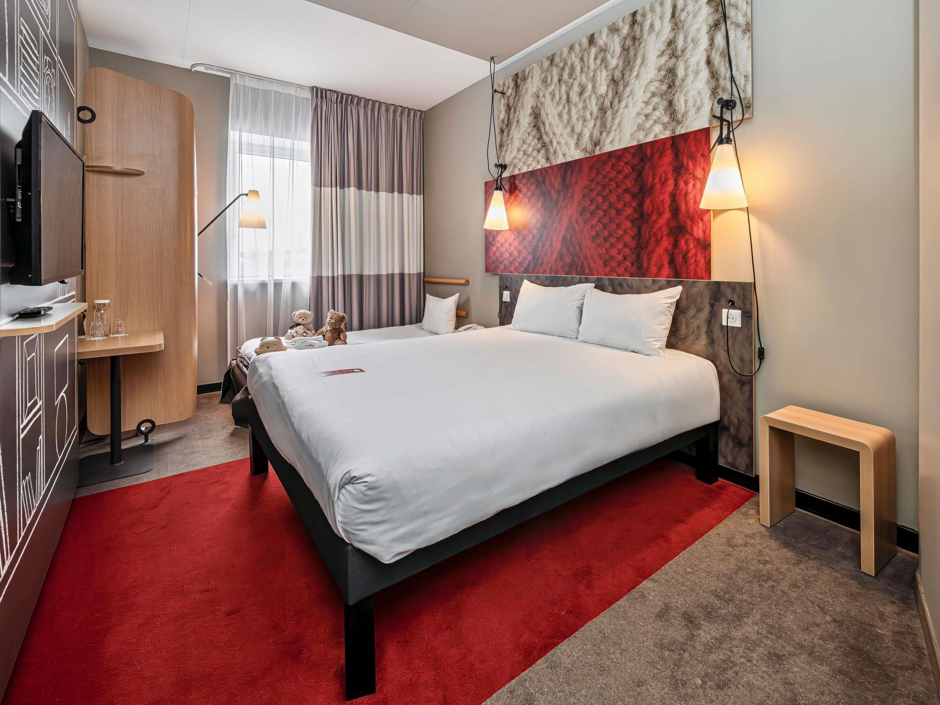 Habitación de hotel con cama, lámparas de noche, escritorio, silla y alfombra roja.