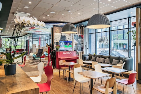 A modern interior with a piano, seating areas, and large windows.. ibis Vilnius Centre