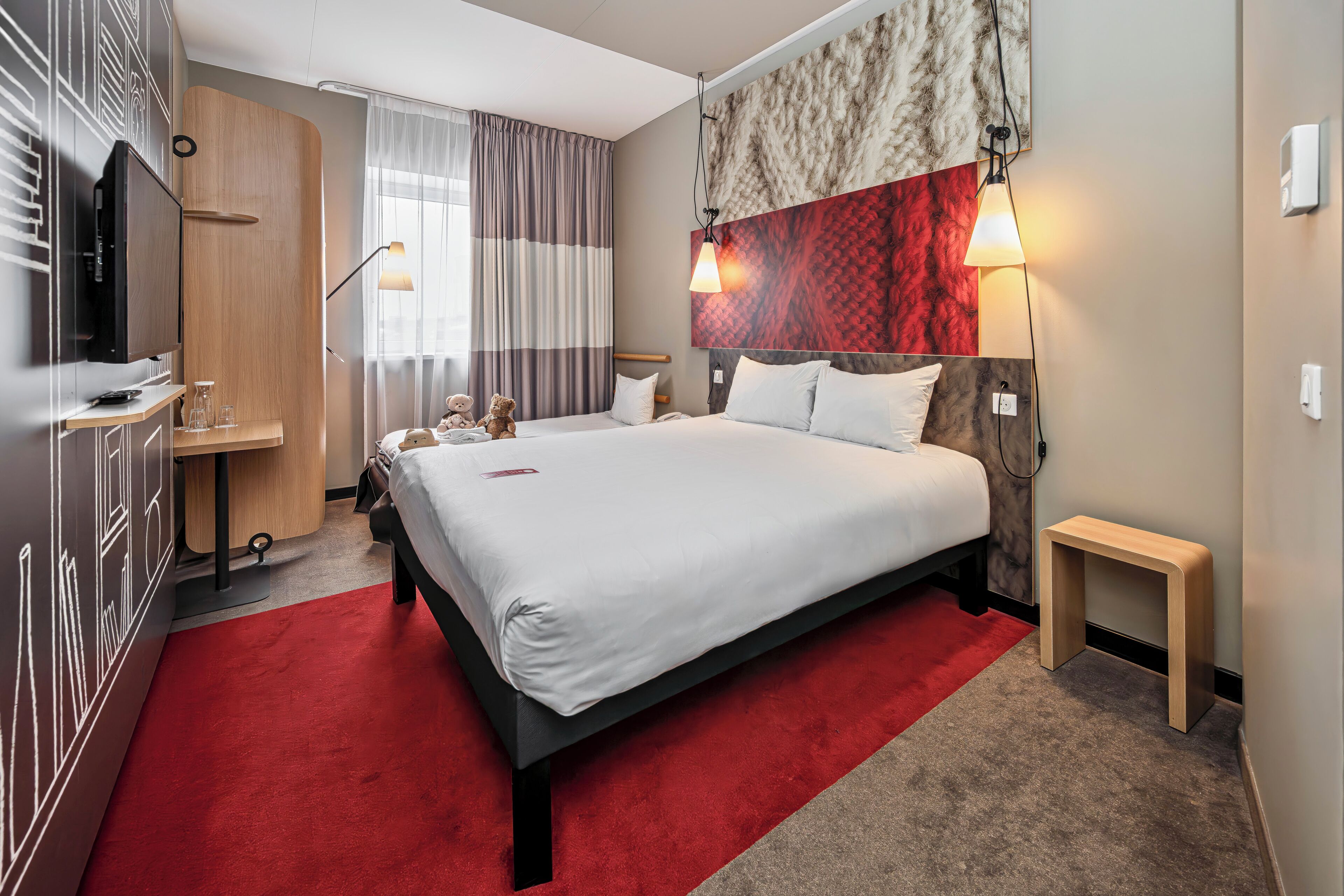 A hotel room with a bed, bedside table, lamp, and a TV.