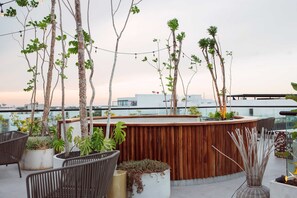 Una terraza en la azotea con asientos de madera, plantas en macetas y una zona de bar de madera.