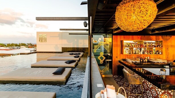 Eine Dachterrasse mit Pool, Liegestühlen und einer Bar mit Flaschen.
