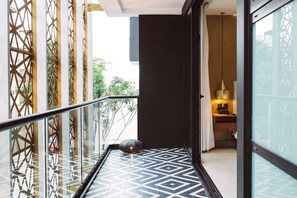 A modern hotel corridor with geometric patterned flooring, a glass door leading to a room with a bed and a nightstand, and a decorative lamp. - IT Boutique Hotel & Restaurant (Playa del Carmen)