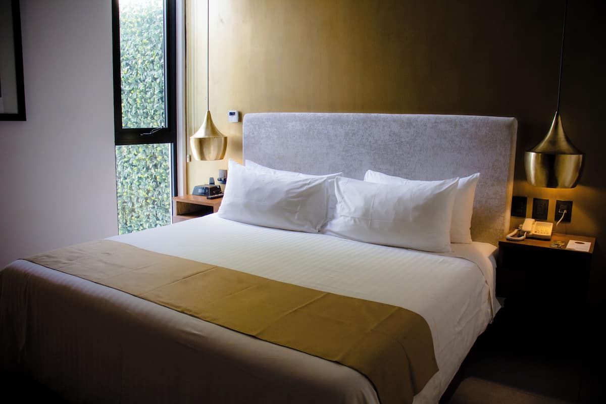 Una cama bien hecha con sábanas blancas, una lámpara de noche y un teléfono en la mesita de noche.
