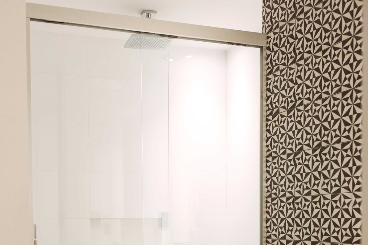 A bathroom with a glass shower enclosure, a toilet, and a patterned wall.