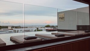 A modern rooftop pool area with glass walls, a lounge with cushions, and a view of the cityscape. - IT Boutique Hotel & Restaurant (Playa del Carmen)
