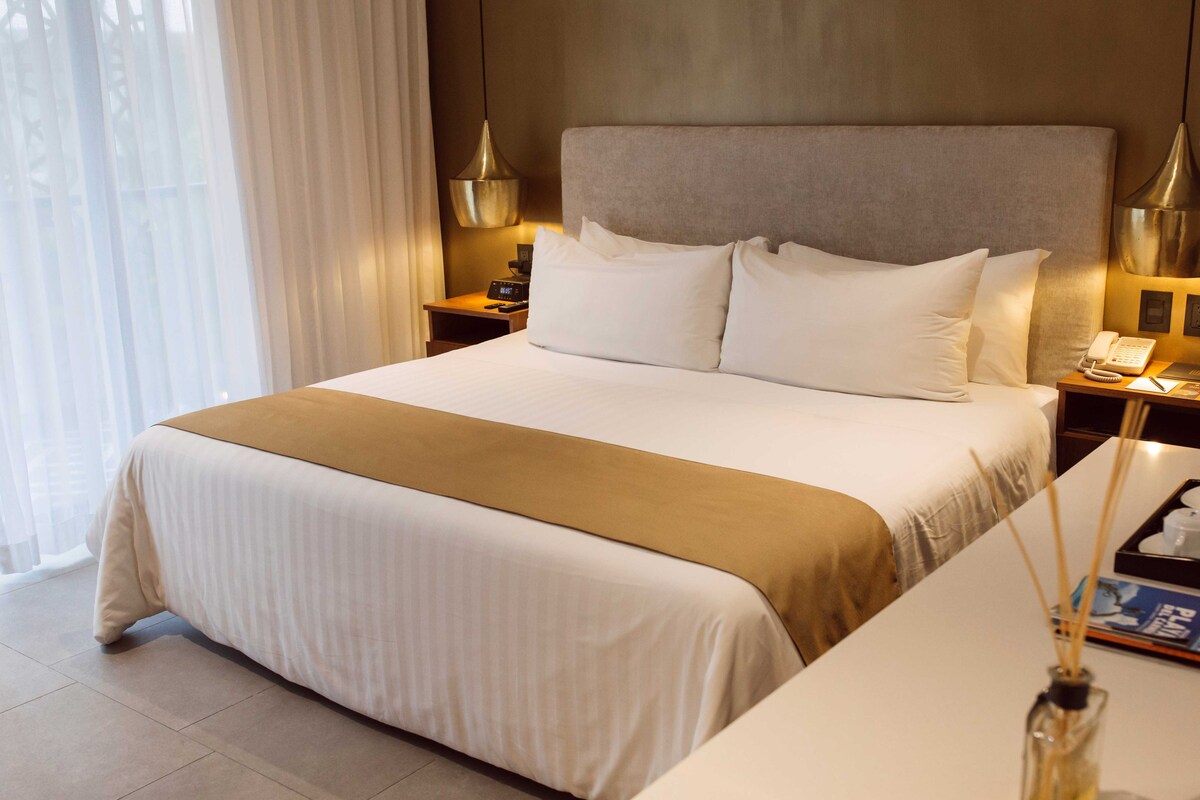 A hotel room with a large bed, bedside tables, a nightstand, a lamp, and a window with curtains.