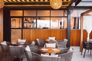 Relax in a charming outdoor seating area with tables, wicker chairs, and a view of the street.