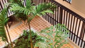 Un espacio interior de varios niveles con un atrio central que presenta un suelo con diseño, barandillas negras y abundante vegetación verde.