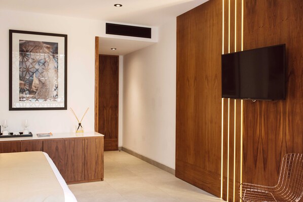 Ein modernes Hotelzimmer mit einer Wandpaneele aus Holz, einem flachbildfernseher an der Wand, einem Bett mit weißem Kopfteil und einem Schreibtisch mit Spiegel und gerahmtem Bild.