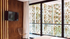 Ein modernes Hotelzimmer mit großem Fenster, einem Wand-Fernseher, einem Bett und einem Sessel.