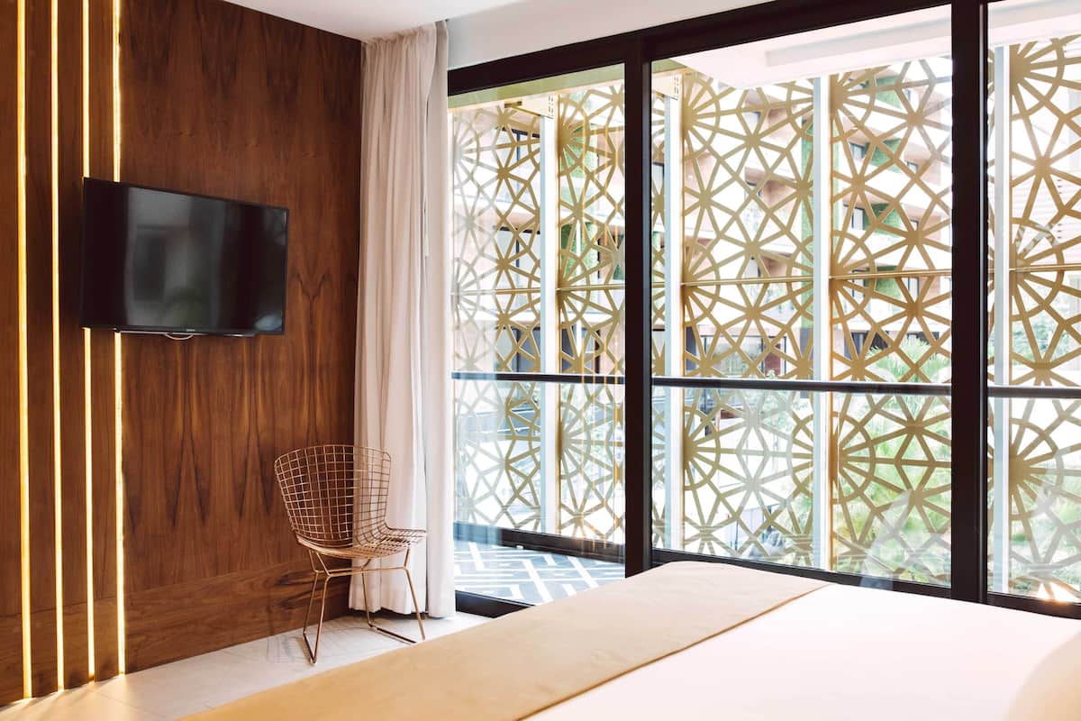 Una habitación de hotel moderna con un ventanal grande, un televisor de pantalla plana en la pared, una cama y una silla.