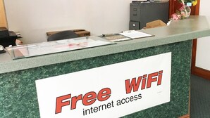 A reception desk with a sign offering free WiFi and internet access. - Village Motel (Ellenville)