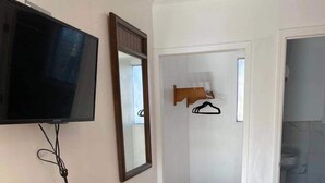 A room with a wooden table, a black office chair, a flat-screen TV, a mirror, and a door leading to a bathroom. - Village Motel (Ellenville)