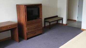 A hotel room with a bed, a wooden TV stand, a bench, and a desk.