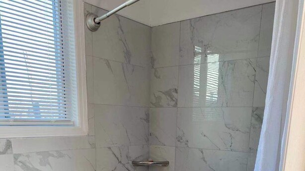 A bathroom with a toilet, a shower with a grab bar, and a wheelchair-accessible bench. - Village Motel (Ellenville)