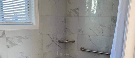 Une salle de bain équipée de toilettes, d’une douche avec une barre d’appui et d’un banc accessible aux personnes en fauteuil roulant.