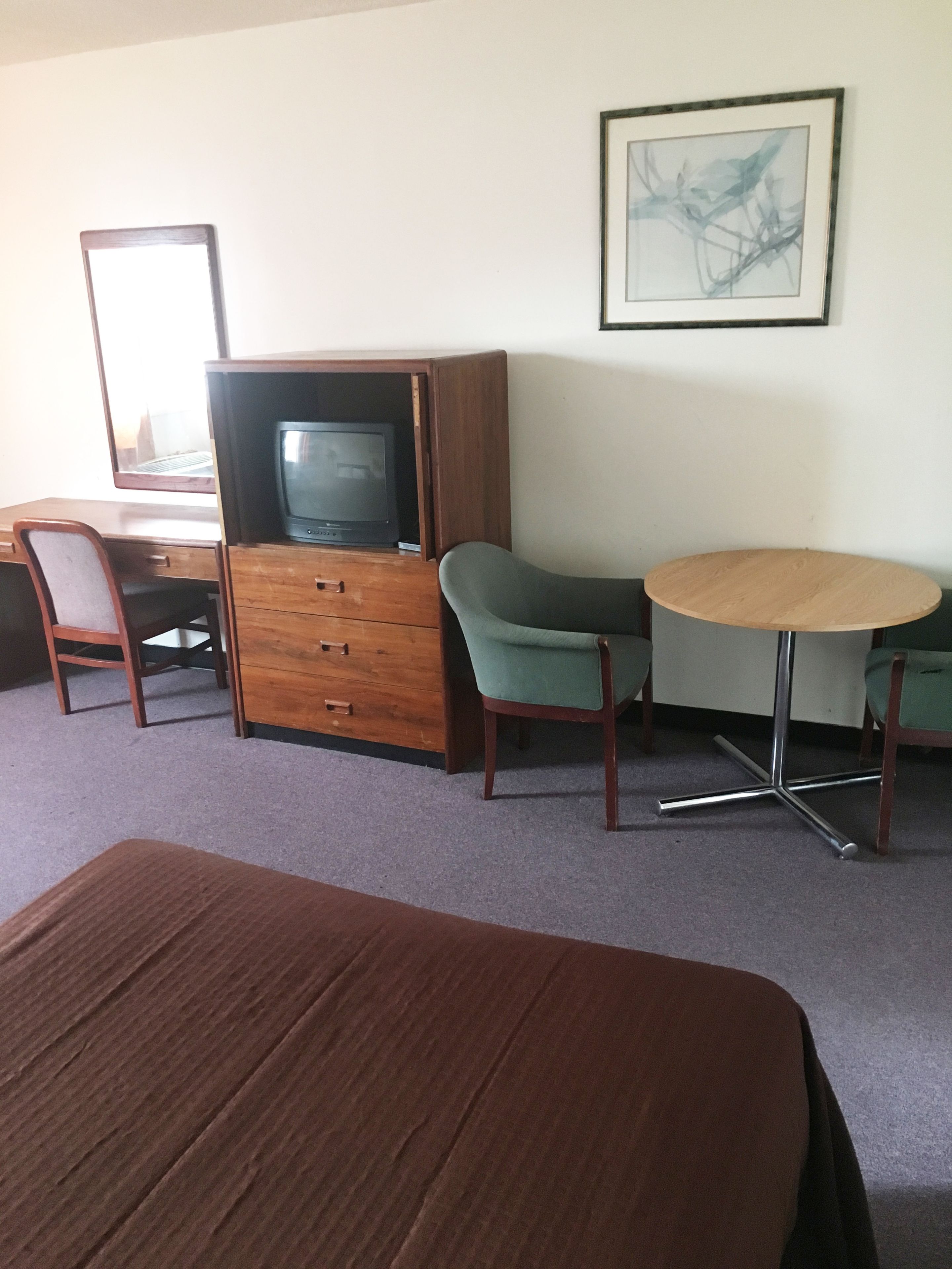 A room with a bed, a wooden dresser, a television, a desk, two chairs, and a round table.