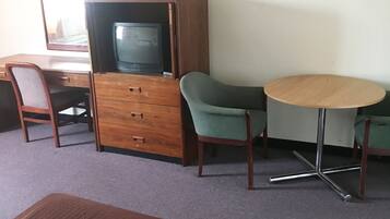 A room with a bed, a wooden dresser, a television, a desk, two chairs, and a round table.