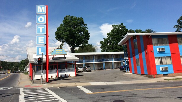 A motel with a prominent blue sign, a covered parking area, and a building with red and blue exterior walls. - Village Motel (Ellenville)