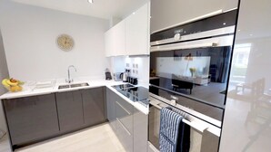 A modern kitchen with a built-in oven, a sink, and a clock on the wall. - Signet Apartments-Vesta (Cambridge)