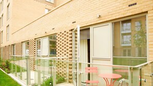 A modern building with a glass balcony, red chairs, and a small table. - Signet Apartments-Vesta (Cambridge)