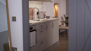 A narrow hallway leading to a kitchen with wooden cabinets, a sink, and a dining area with a table and chairs.