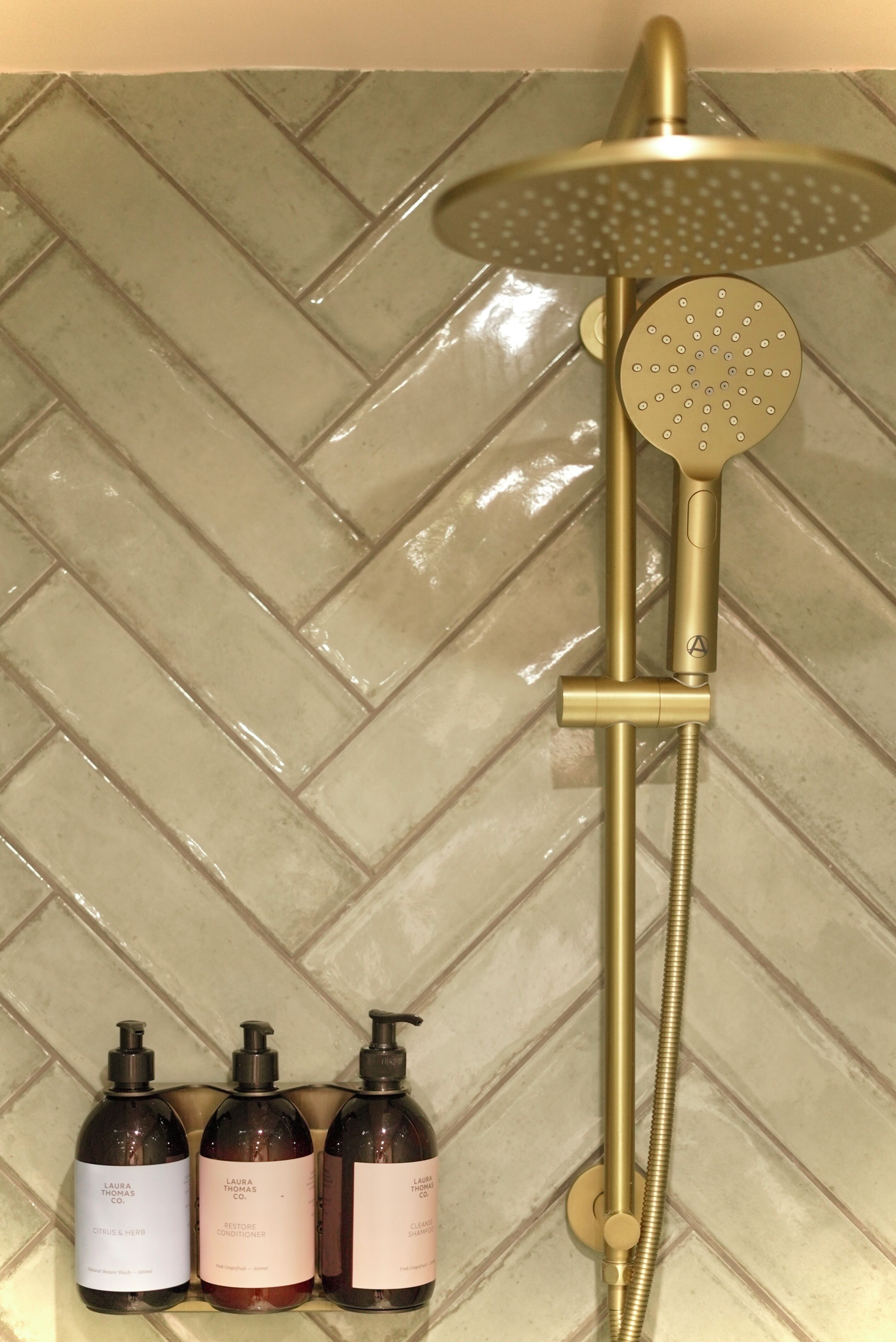 A shower with a gold showerhead and hose, set against a herringbone tile backsplash.