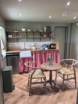 Une cuisine avec des étagères en bois, un évier et un coin repas comprenant une table et des chaises.