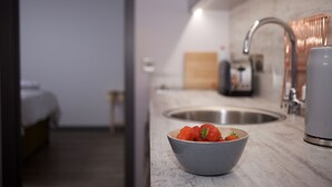 A modern kitchen with a bowl of strawberries on the counter, a sink, and a coffee machine.