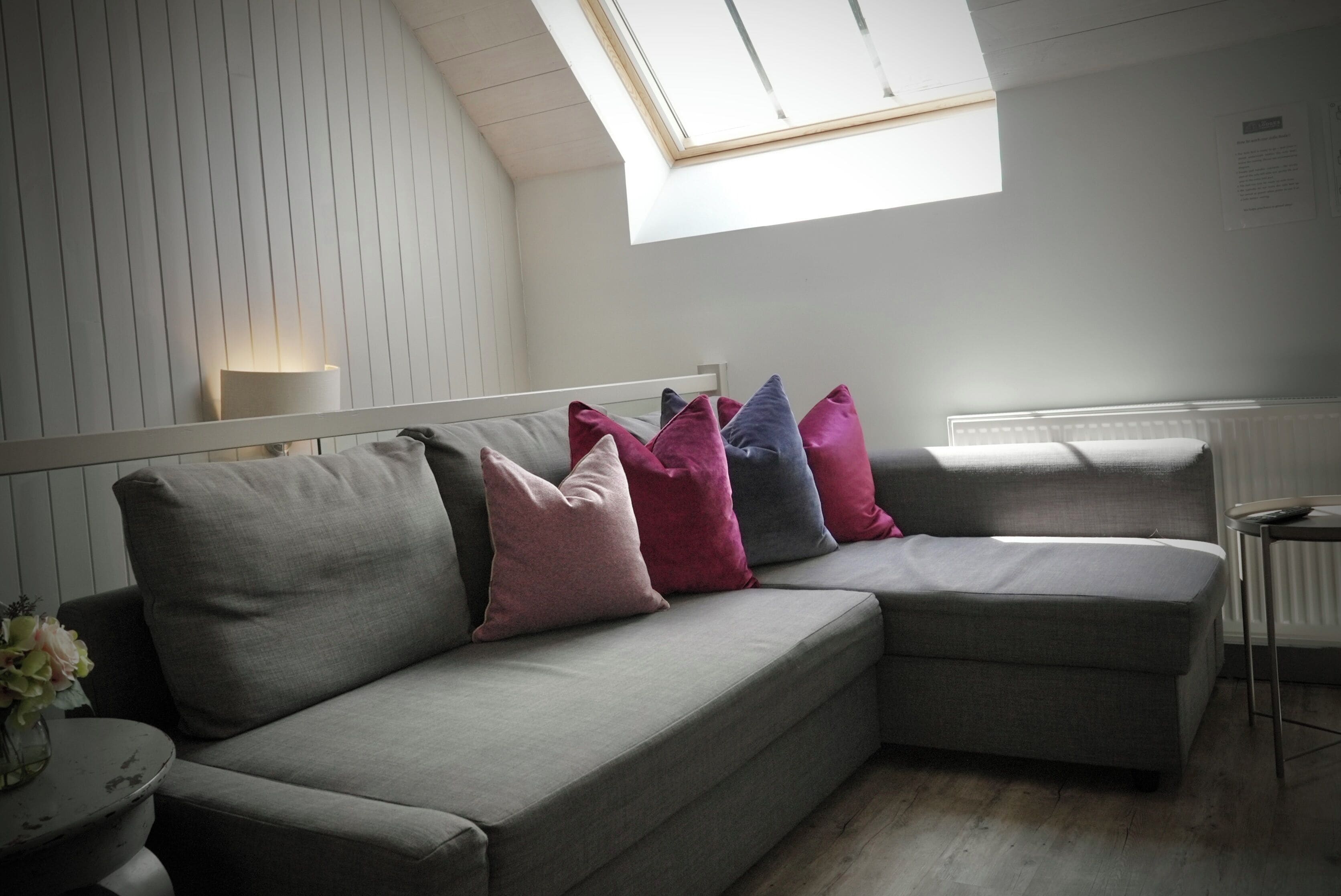 A modern living room with a grey sectional sofa, a small round table, and a skylight.