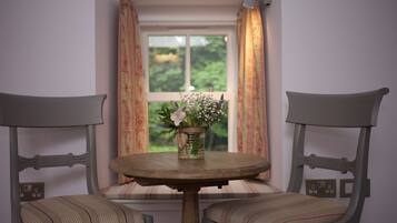 Una habitación con una mesa redonda y dos sillas con cojines a rayas. Un jarrón con flores está sobre la mesa.