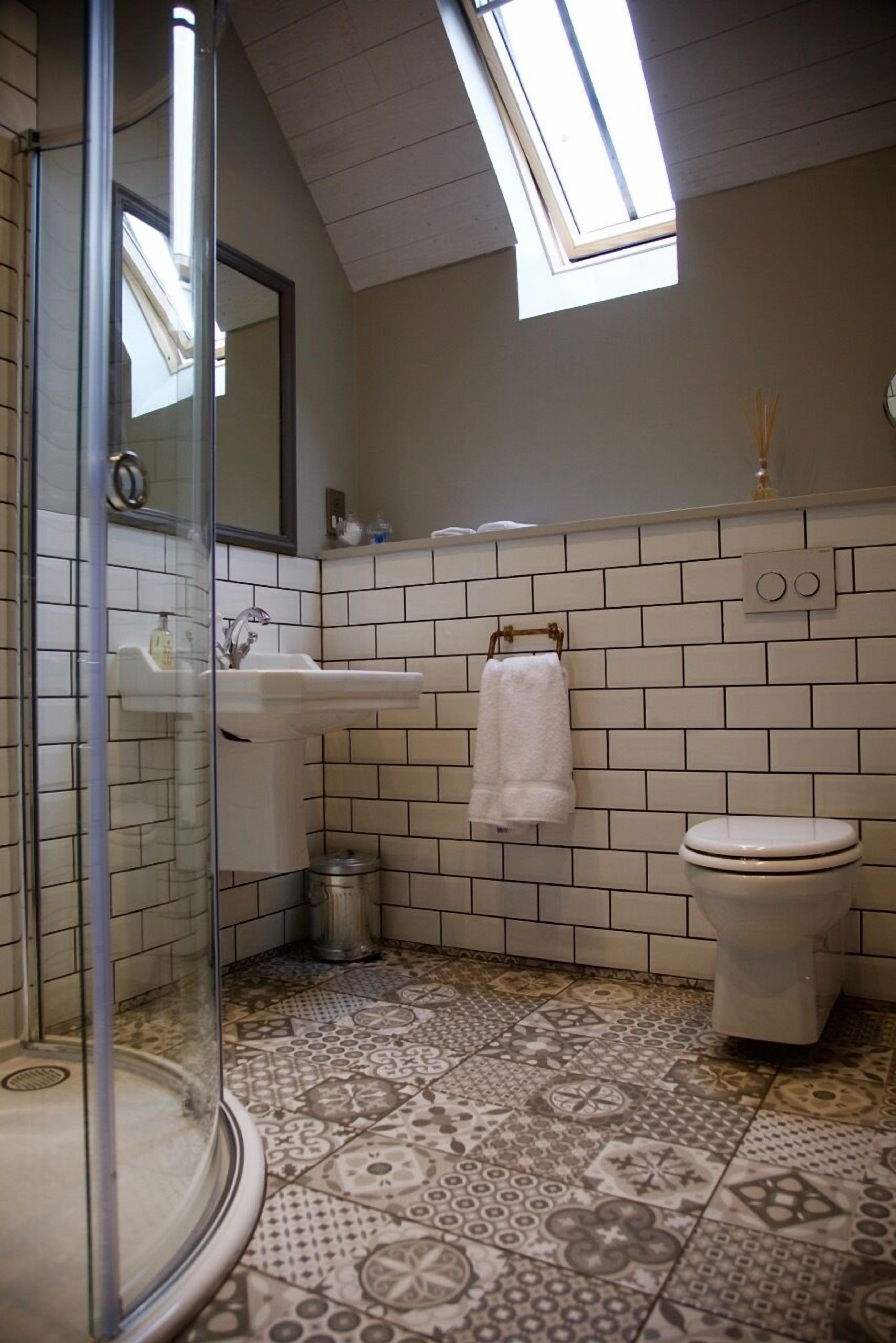 Un baño con ducha, lavamanos, inodoro y baldosas de suelo estampadas.