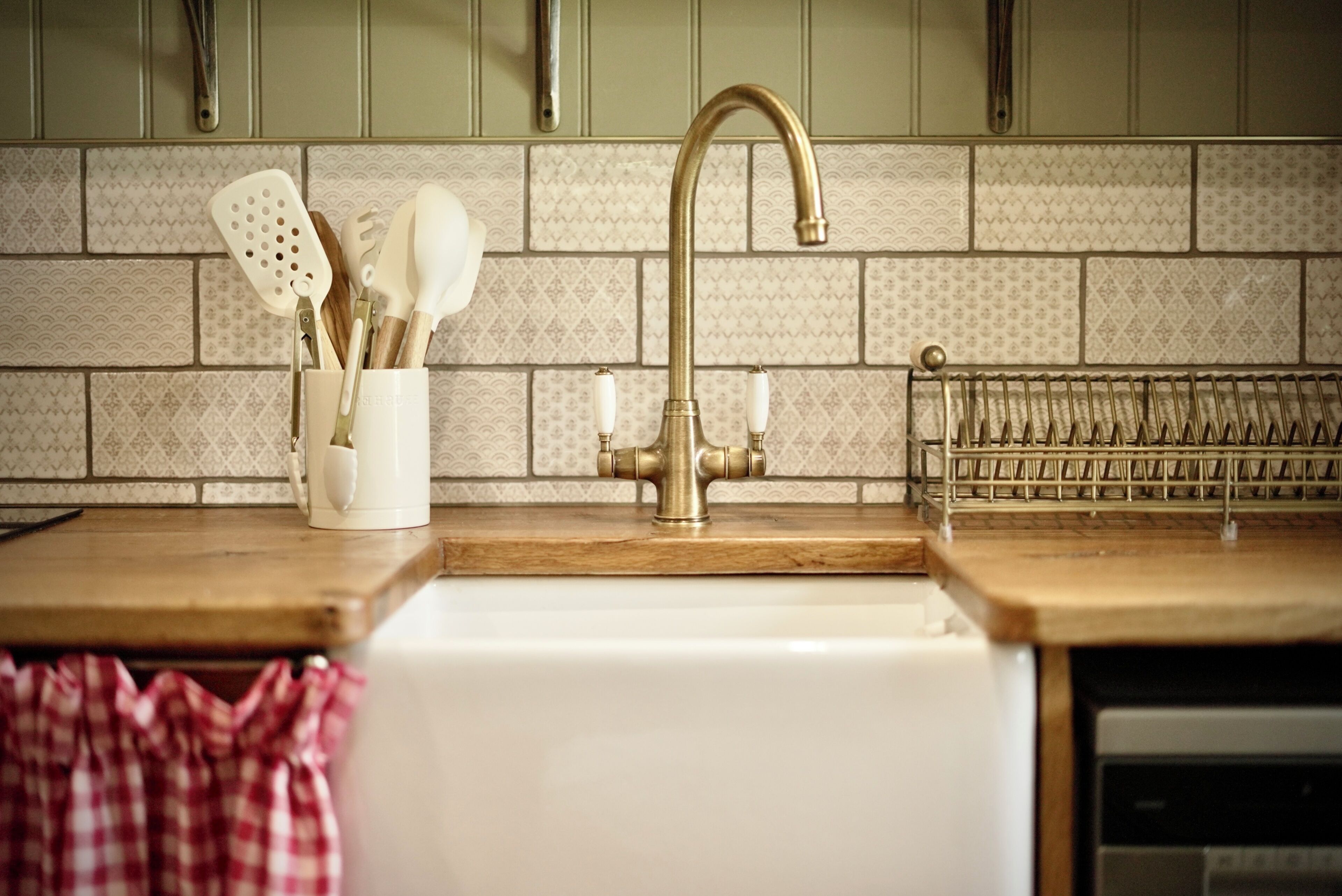 A kitchen with a sink, a faucet, and a utensil holder with spoons and spatulas.