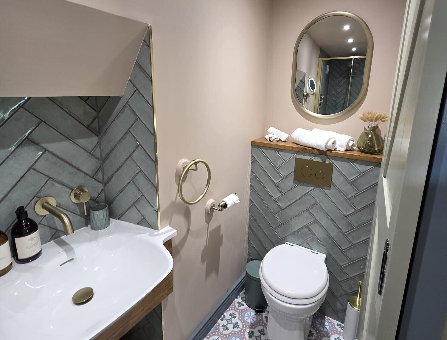 Un baño con salpicadero de azulejos tipo espiga, un lavabo blanco con detalles dorados, un inodoro y un espejo con marco dorado.
