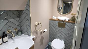 Un baño con salpicadero de azulejos tipo espiga, un lavabo blanco con detalles dorados, un inodoro y un espejo con marco dorado.
