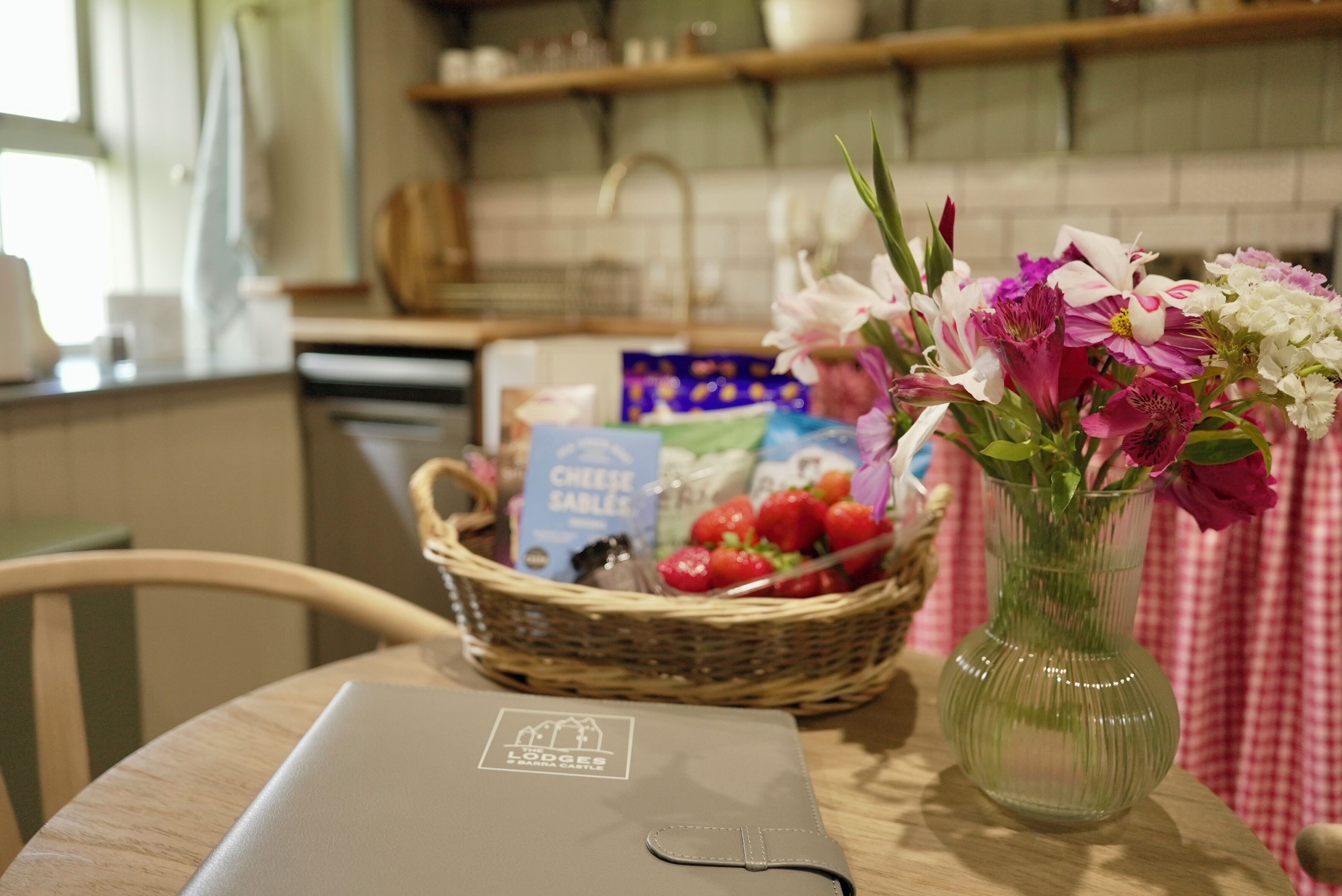 Una cucina con un portatile su un tavolo, un cesto di fragole e un vaso con fiori.
