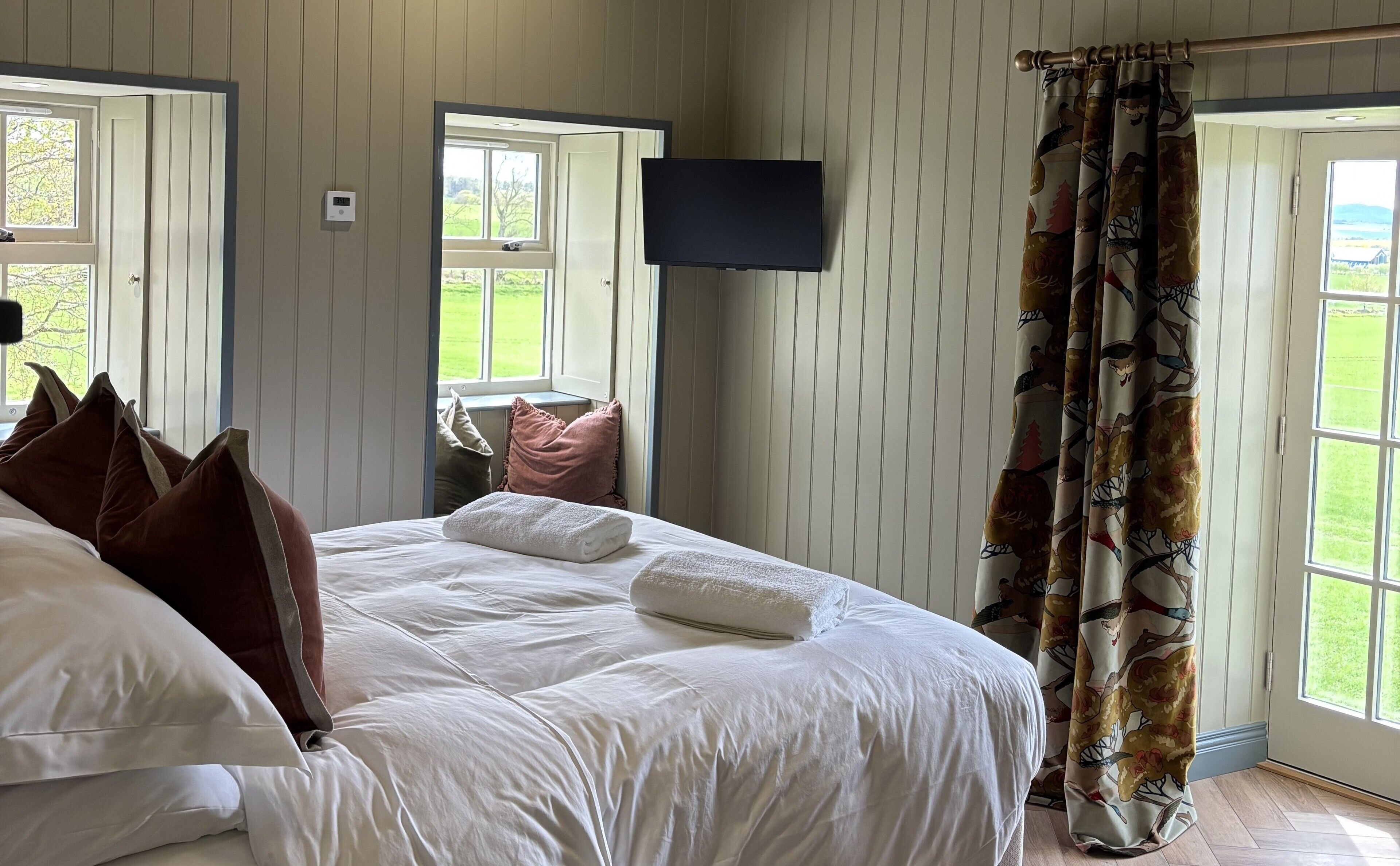 A bedroom with a bed, pillows, a TV, and a window with curtains.