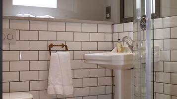 Un baño con tragaluz, paredes de azulejos blancos, un lavamanos, un inodoro y baldosas de suelo estampadas.