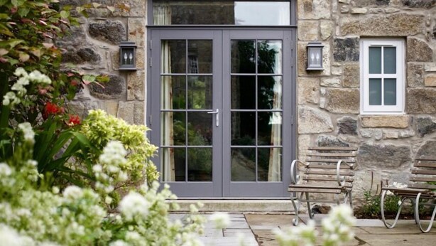 A stone building with a large grey door and a small window.