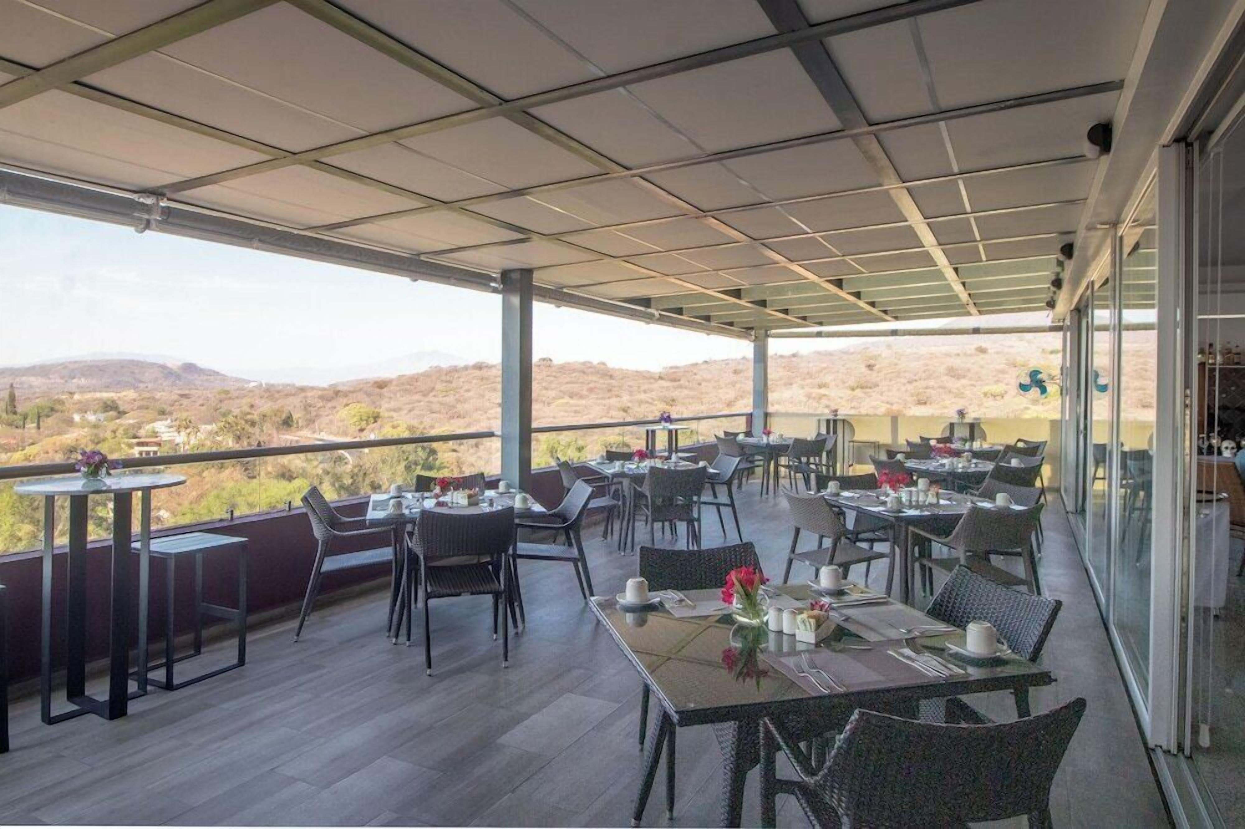 Un área de comedor al aire libre con mesas y sillas, con vistas a un paisaje desértico.