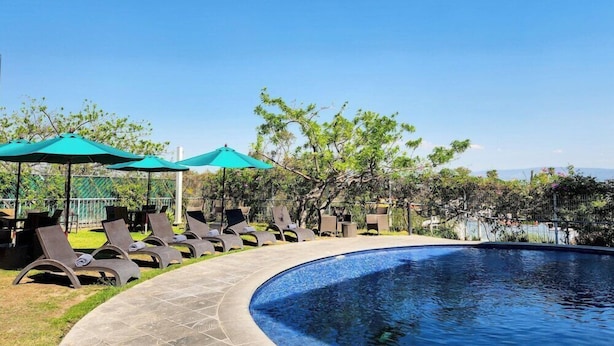 A poolside area with lounge chairs and umbrellas, surrounded by trees and a clear sky. - Gamma Chapala (Chapala)