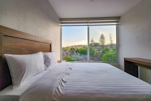 A bedroom with a large window, a wooden headboard, and a bed with white bedding. - Gamma Chapala (Chapala)