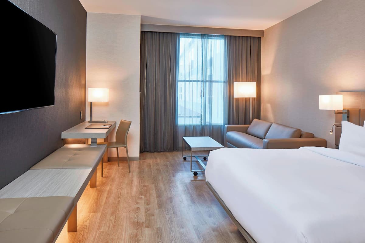 Ein Hotelzimmer mit einem großen Bett, einer Couch, einem Schreibtisch mit Stuhl, einem Fernseher und zwei Lampen.